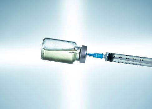 Macro of a hypodermic syringe or needle being filled with vaccine from bottle against a blue star background