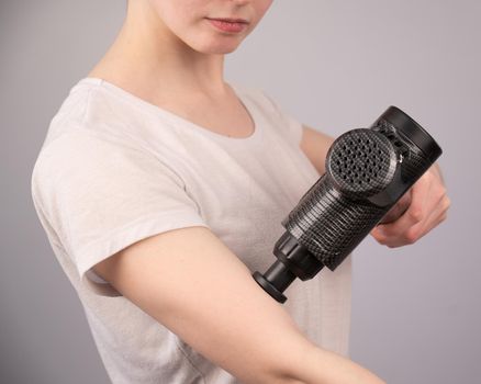 Caucasian woman uses a massager gun for pain in the muscles of the arm