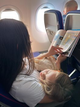 Mom with a sleeping daughter sits in an airplane seat and reads a magazine. High quality photo