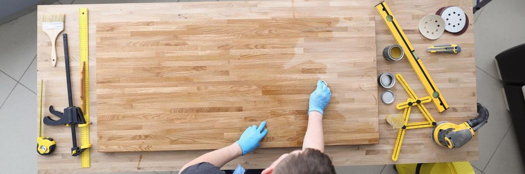 Top view of carpenter handy man lacquer wooden plank at workroom. Worker cover wood part of furniture with shiny varnish. Construction, renovation concept