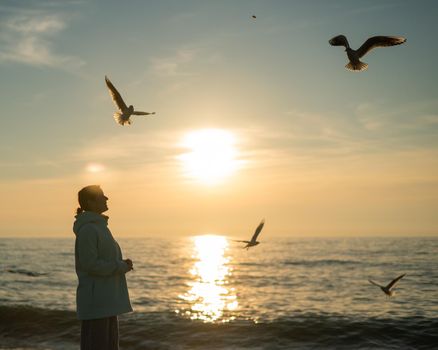 Caucasian woman feeding seagulls at sunset by the sea