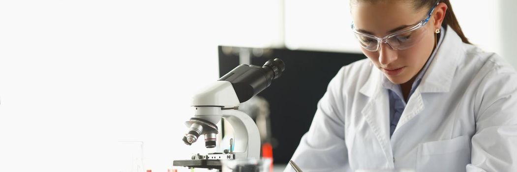 Portrait of concentrated chemist worker write down thoughts on investigation project in lab. Biologist examine samples in modern clinic. Science concept