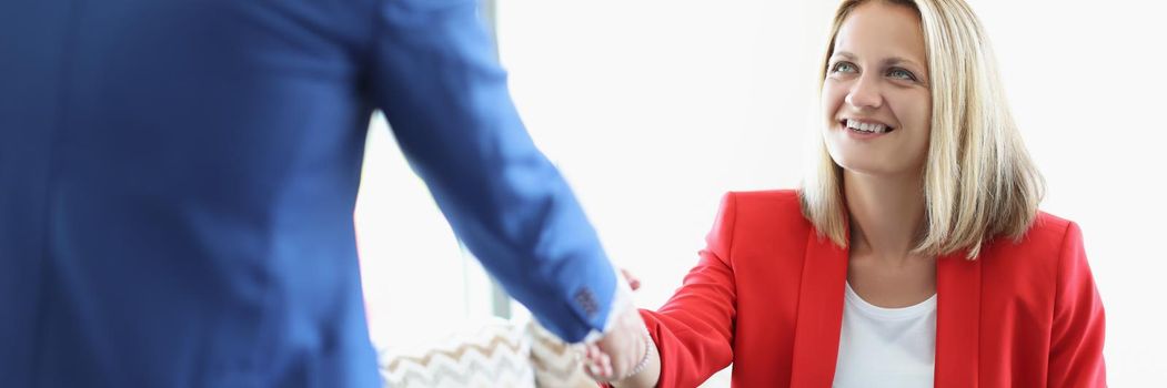 Portrait of cheerful blonde young lady greeting man with handshake sitting on sofa. Business meeting to discuss agreement. Deal, lunch time, career concept