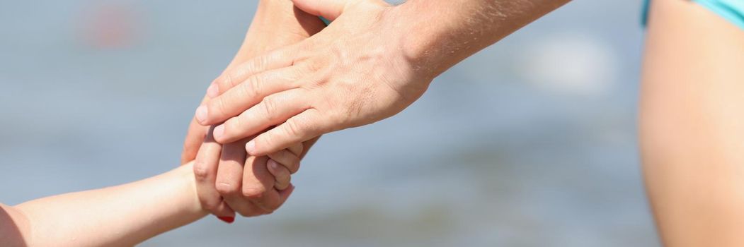Close-up of family holding hands, mother father and child walking on coastline. Cropped picture of warm and lovable relationships in family. Love concept
