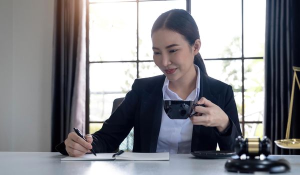 Professional Asian female lawyer working in her office, sipping a morning coffee while reading a law contract. cropped image.