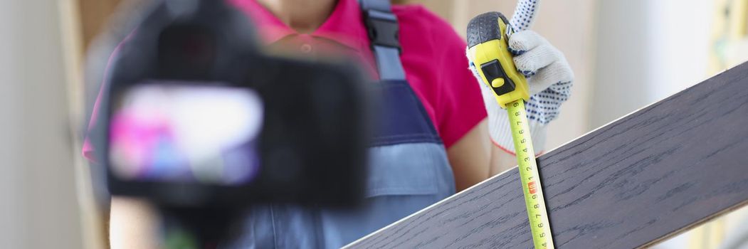 Portrait of smiling woman construction site worker measure plank with tape measure tool. Woman film educational lesson. Renovation, social media concept