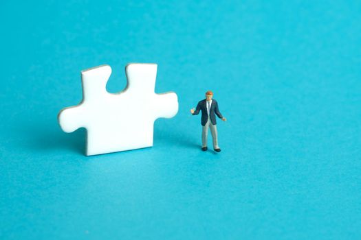 Miniature people toy figure photography. A shrugging businessman standing in front of puzzle jigsaw piece. Isolated on blue background. Image photo