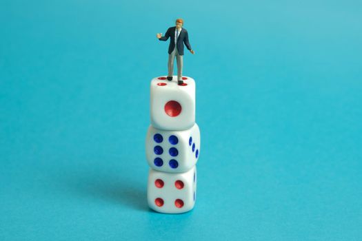 Miniature people toy figure photography. A shrugging businessman standing above white dice. Isolated on blue background. Image photo