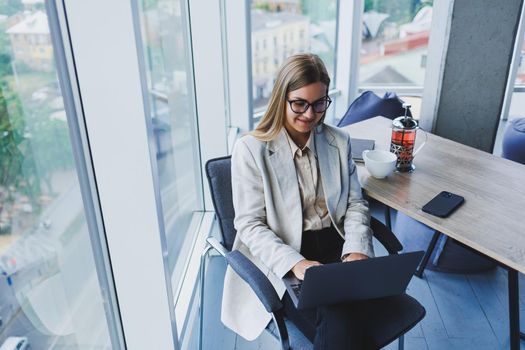 Smiling business woman looking at laptop while working in office. The concept of a modern successful woman. The idea of business and life of an entrepreneur. Young woman at table with open laptop