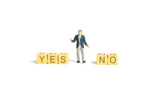 Miniature people toy figure photography. A shrugging businessman standing in the middle of yes and no  wooden cube block. Isolated on white background. Image photo