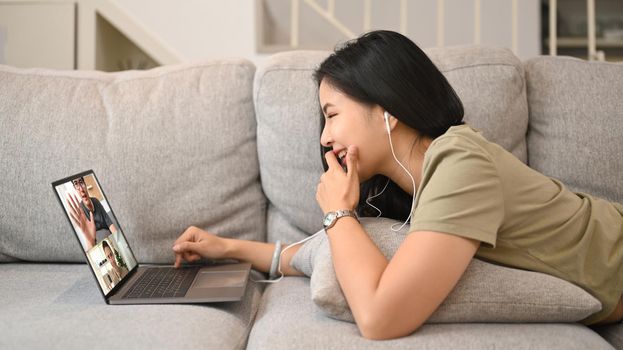 Young woman in casual wears lying on couch and communication through video chat.