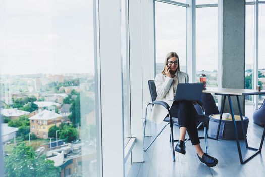 Smiling business woman looking at laptop while working in office. The concept of a modern successful woman. The idea of business and life of an entrepreneur. Young woman at table with open laptop