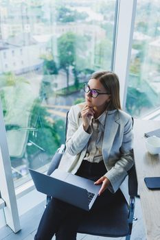 Smiling business woman looking at laptop while working in office. The concept of a modern successful woman. The idea of business and life of an entrepreneur. Young woman at table with open laptop