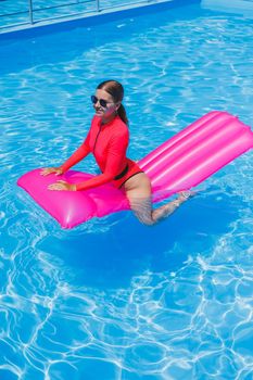 Beautiful girl in a pink swimsuit relaxing on an inflatable pink mattress in the pool. A slender hot woman in sunglasses and swimsuits is sunbathing. A woman is relaxing in a luxury resort.