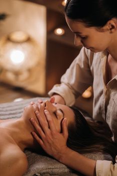 A cosmetologist girl does a facial and neck massage to a girl in the office for skin elasticity.