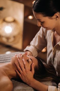 A cosmetologist girl does a facial and neck massage to a girl in the office for skin elasticity.