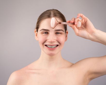 Close-up portrait of a woman with braces on her teeth uses a quartz roller massager to smooth wrinkles on her forehead