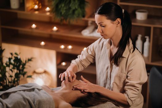 A cosmetologist girl does a facial and neck massage to a girl in the office for skin elasticity.