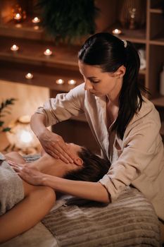 A cosmetologist girl does a facial and neck massage to a girl in the office for skin elasticity.