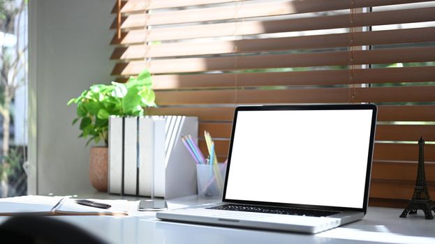 Computer laptop, books, coffee cup and houseplant beside the window with sunlight shine through the curtain.