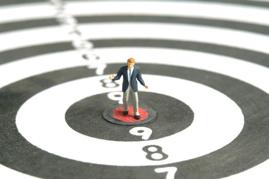 Miniature people toy figure photography. A shrugging businessman standing the center of dartboard. Isolated on white background. Image photo