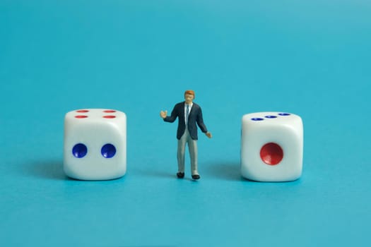 Miniature people toy figure photography. A shrugging businessman standing in the middle of white dice. Isolated on blue background. Image photo