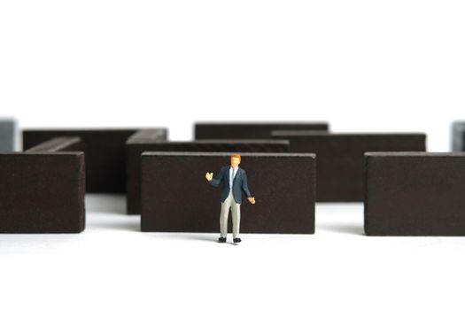 Miniature people toy figure photography. Strategy choice concept. A shrugging businessman standing in front of wooden maze labyrinth. Isolated on white background. Image photo