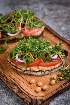  Sandwich toasted rustic bread with chickpea hummus, tomato slices, mix of lettuce and microgreens. Vegetarian breakfast. 