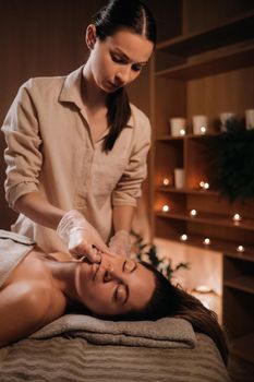 A cosmetologist girl does a facial and neck massage to a girl in the office for skin elasticity.