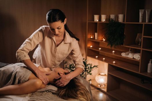 A masseuse gives a body massage to a woman in a spa center. A professional masseur massages the shoulder of a girl lying in a spa center.