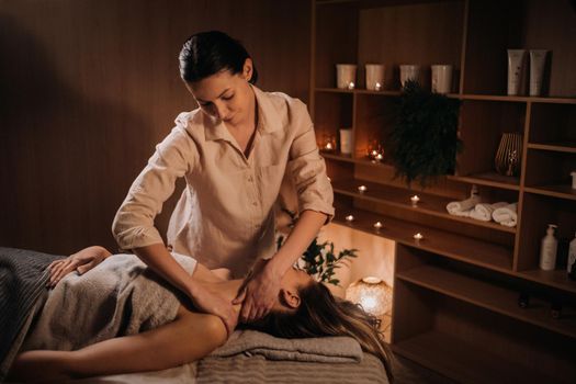 A masseuse gives a body massage to a woman in a spa center. A professional masseur massages the shoulder of a girl lying in a spa center.