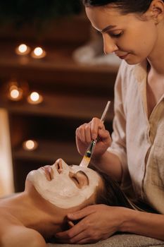 A cosmetologist makes a mask for a woman's face to rejuvenate the skin. Cosmetology.