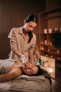 A cosmetologist girl does a facial and neck massage to a girl in the office for skin elasticity.