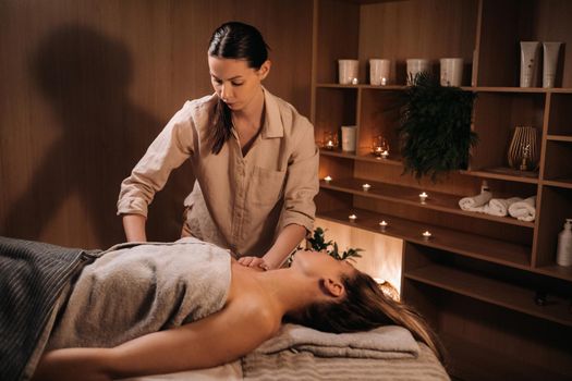 A masseuse gives a body massage to a woman in a spa center. A professional masseur massages the shoulder of a girl lying in a spa center.