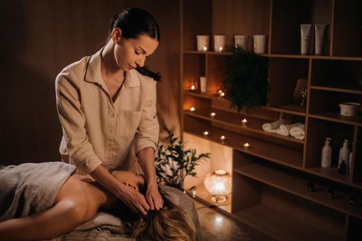 A masseuse gives a body massage to a woman in a spa center. A professional masseur massages the shoulder of a girl lying in a spa center.