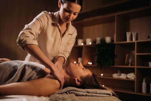 A masseuse gives a body massage to a woman in a spa center. A professional masseur massages the shoulder of a girl lying in a spa center.