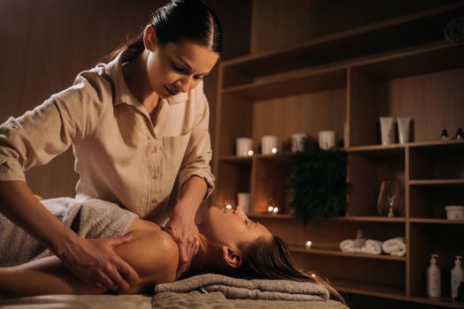 A masseuse gives a body massage to a woman in a spa center. A professional masseur massages the shoulder of a girl lying in a spa center.