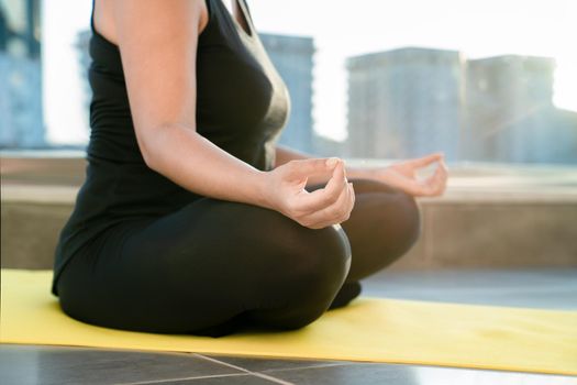 Young woman meditating in lotus position sitting on fitness mat on balcony of her house, close-up. Concept of healthy and harmonious life