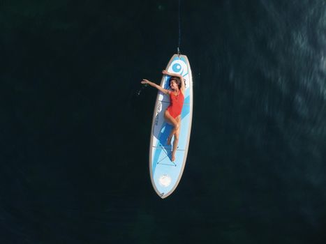 Young attractive brunette woman in red swimsuit, swimming on kayak around volcanic rocks, like in Iceland. Back view. Christmas holiday vacation and travel concept.