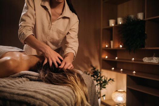 A masseuse gives a head massage to a woman at the spa. A professional masseur massages the head of a girl lying in a spa center.