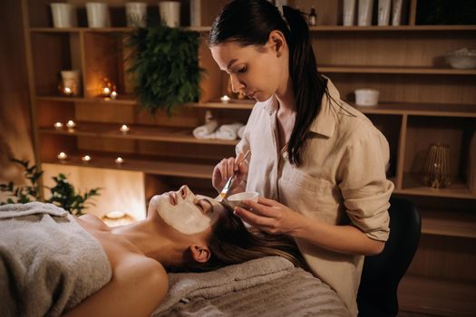 A cosmetologist makes a mask for a woman's face to rejuvenate the skin. Cosmetology.