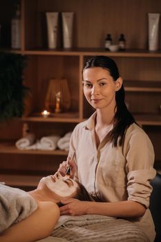 A cosmetologist makes a mask for a woman's face to rejuvenate the skin. Cosmetology.