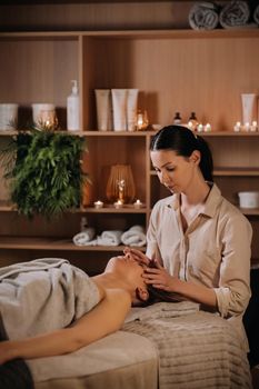 A cosmetologist girl does a facial and neck massage to a girl in the office for skin elasticity.