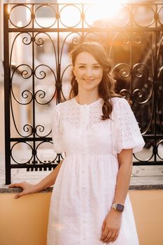 A beautiful woman in a white dress at sunset in the city. Evening street photography.