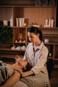 A cosmetologist girl does a facial and neck massage to a girl in the office for skin elasticity.