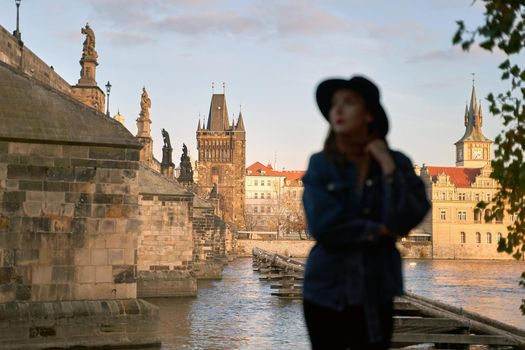 Prague Silhouette. Stylish young woman wearing black hat with Charles Bridge on background. Elegant retro lady fine art portrait. Focus on background.