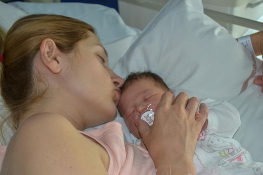 A mother kissing her newborn baby sleep in bed at a hospital.