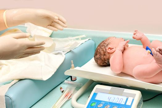 A nurse weighs on the scales a newborn baby