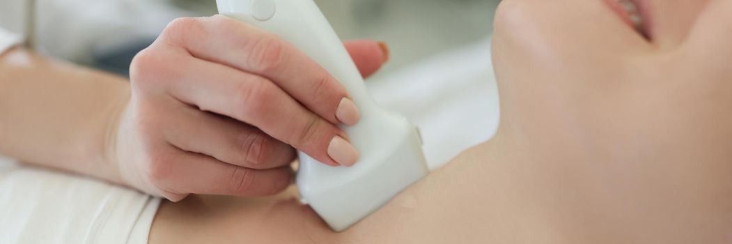 Close-up of ultrasound scanning diagnostic for woman of thyroid gland in hospital, doctor hold ultrasound sensor over neck. Diagnostics, healthcare concept