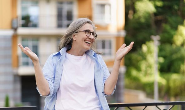 Portrait of mature attractive grey har woman standing outdoors happy spread her hands up in the air. Successful mature business woman happy of signing the contract enjoying moment.